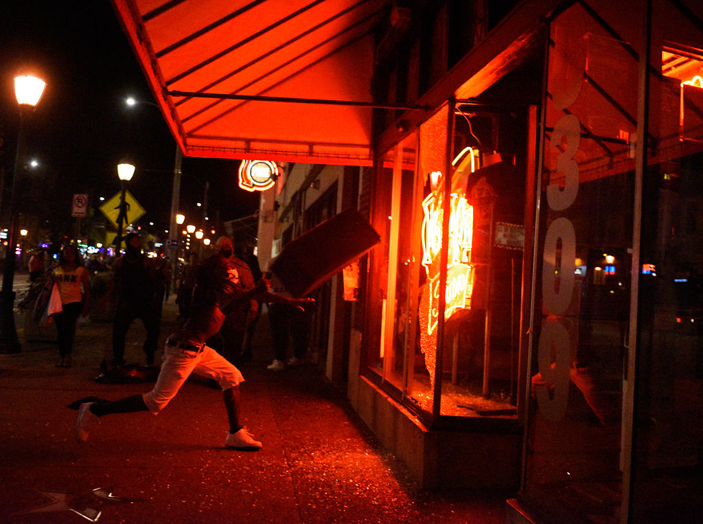 A person throws a trash can through a glass window